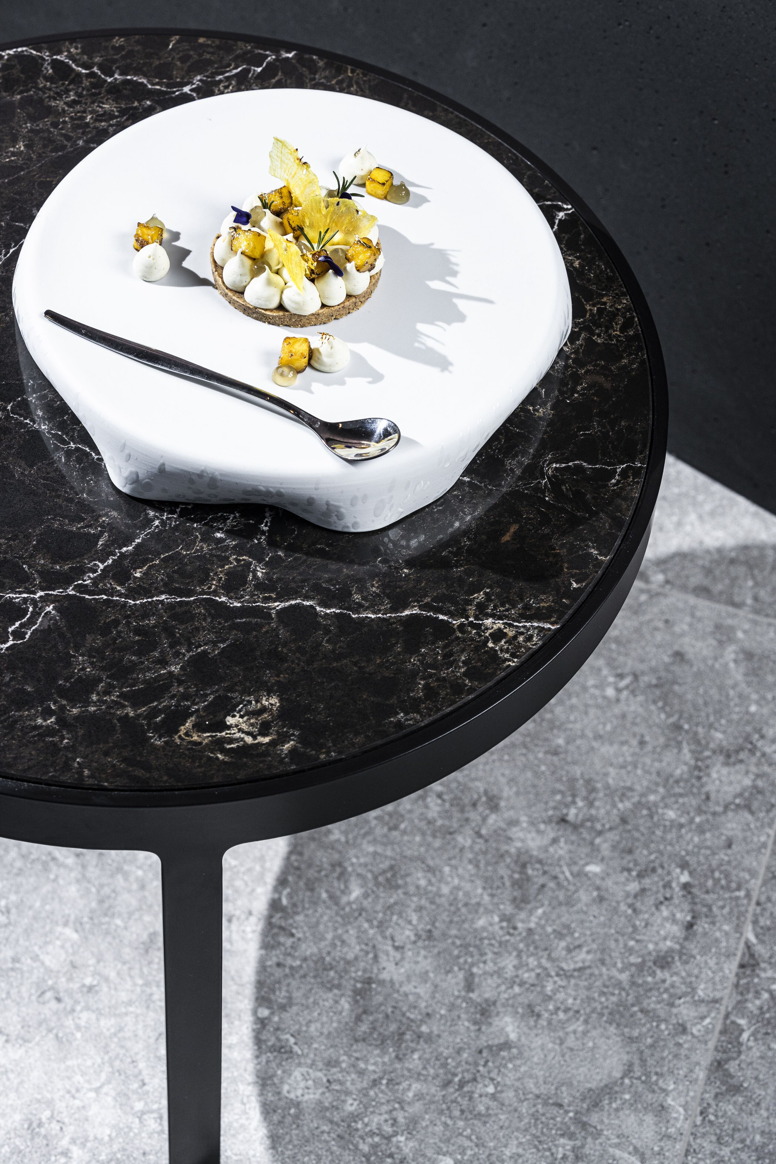 A dessert on a white plate with a spoon, placed on a black marble table.