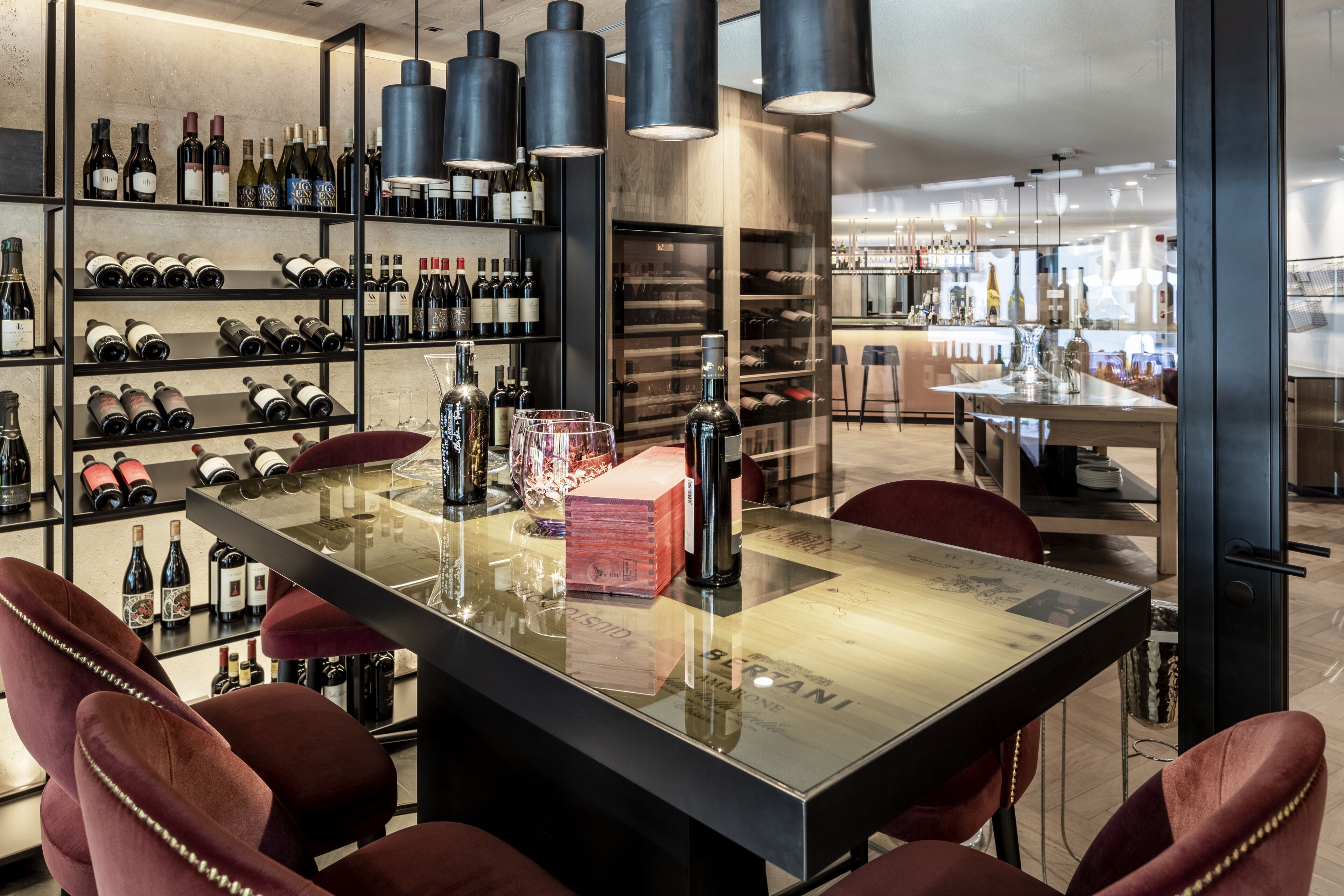 Eine moderne Bar mit einem langen Tisch, roten Sitzmöglichkeiten und Regalen voller Weinflaschen.