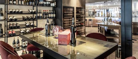 Un espace bar moderne avec une longue table, des chaises à revêtement rouge et des étagères remplies de bouteilles de vin.