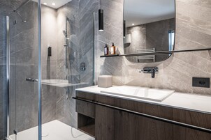 Un baño moderno con ducha envuelta en vidrio, lavamanos blanco y tocador de madera.