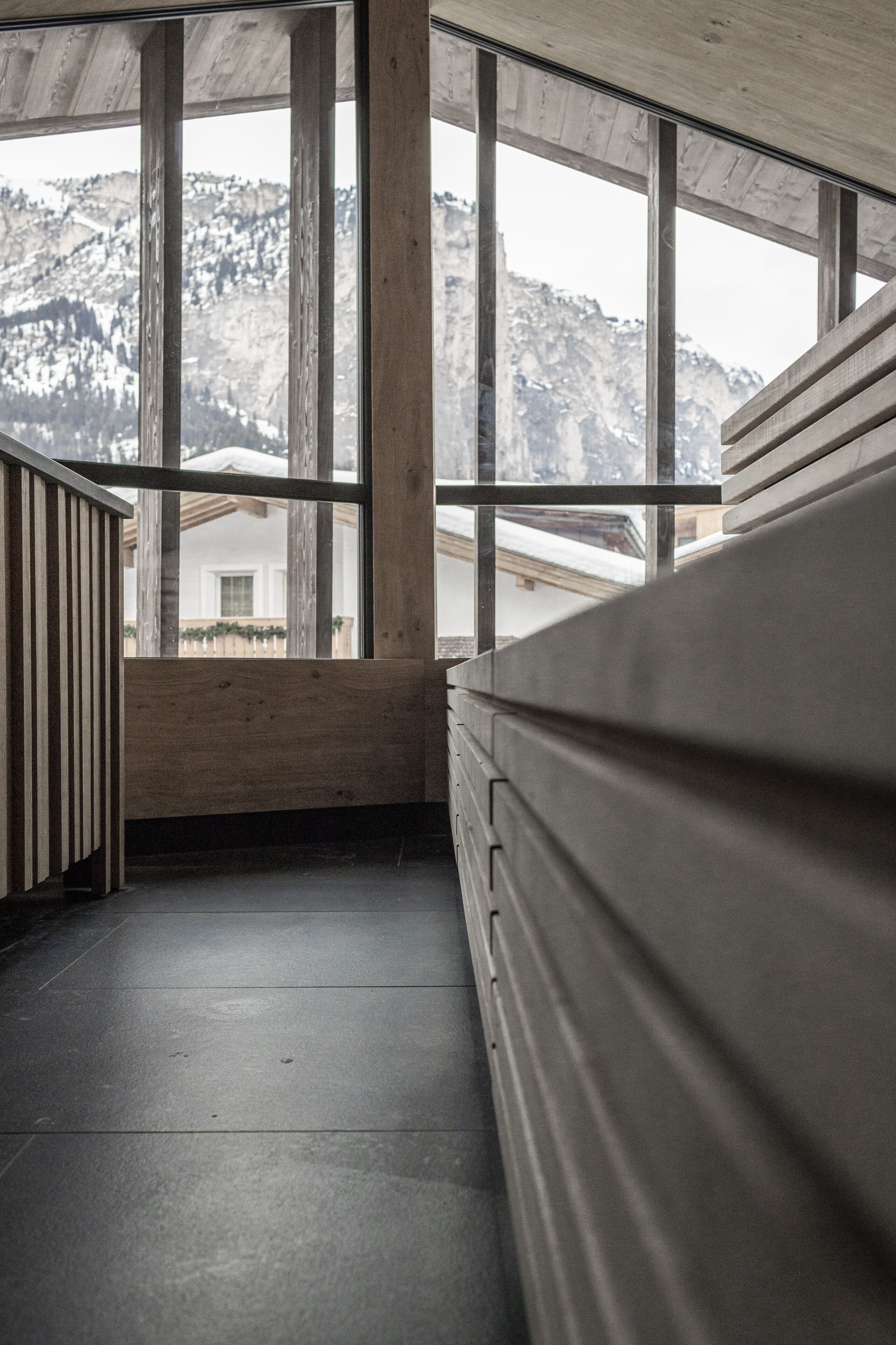 Una escalera de madera que lleva a un balcón con ventanas amplias que dan a un paisaje montañoso.