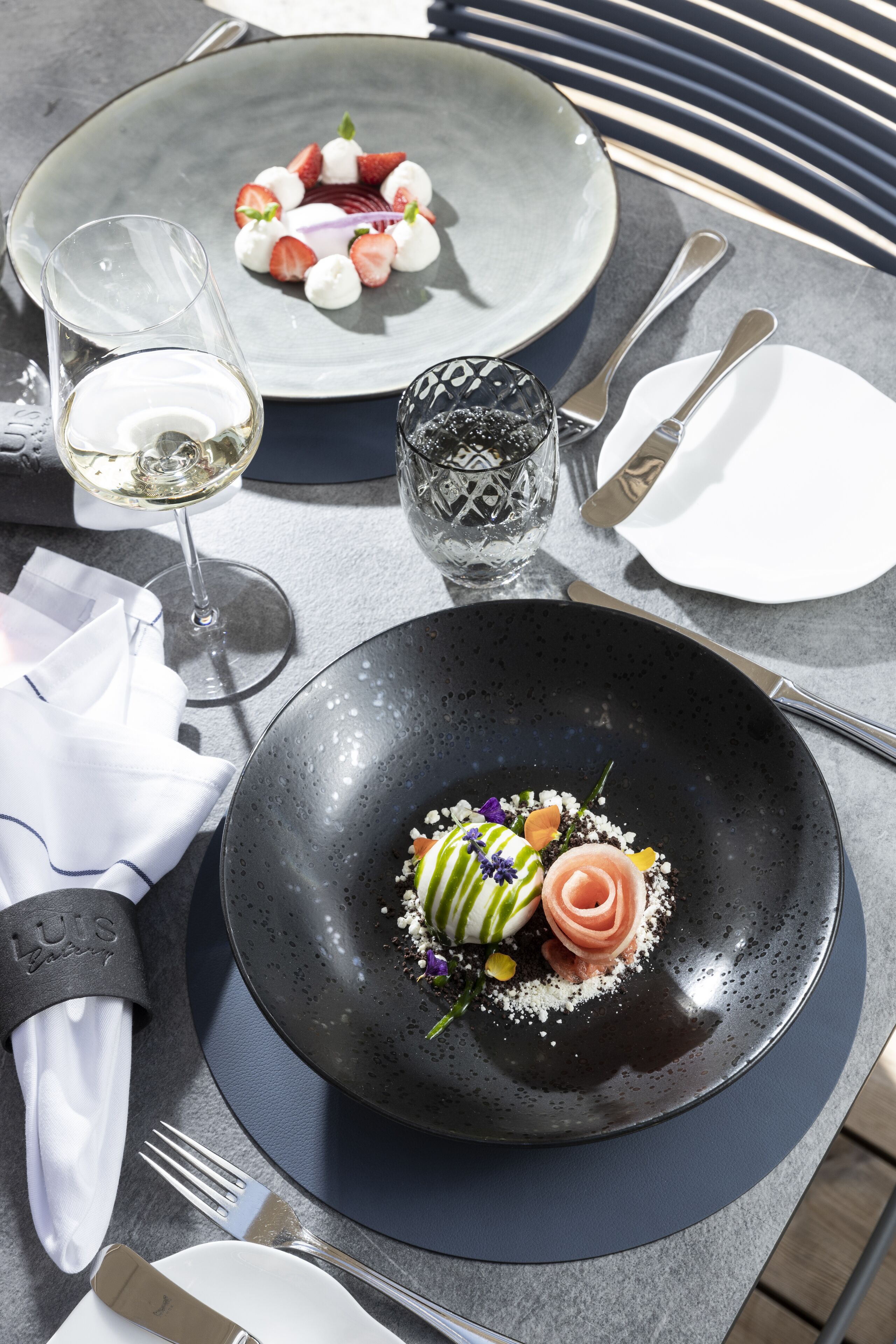 Una mesa de comedor con dos platos de comida, una copa de vino blanco y cubiertos.