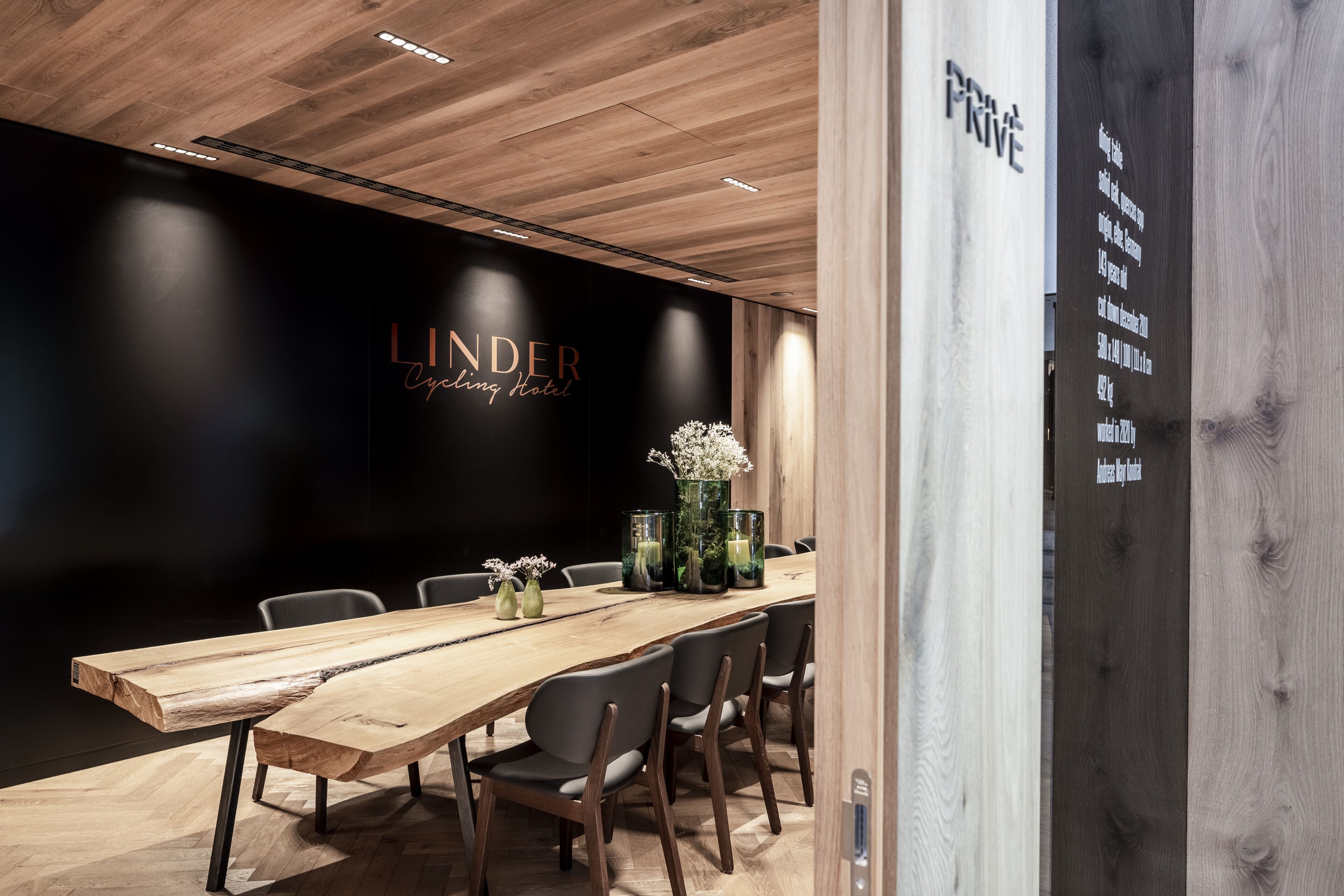 A conference room with a long wooden table, six chairs, and a black wall with the text "LINDER Cycling Hotel".