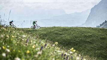 Two cyclists on a grassy hill with mountains in the background.