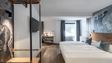 A modern hotel room with a wooden floor, a large bed with white linens, a desk with a chair, a television, and a large abstract painting on the wall.