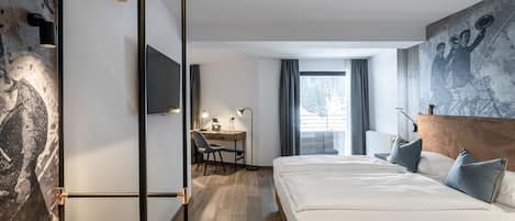Una habitación de hotel moderna con suelo de madera, una cama grande con ropa blanca, un escritorio con silla, un televisor y un cuadro abstracto grande en la pared.