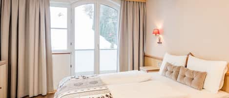 Una habitación de hotel con una cama grande, una mesita de noche, una lámpara y vistas a través de un ventanal.