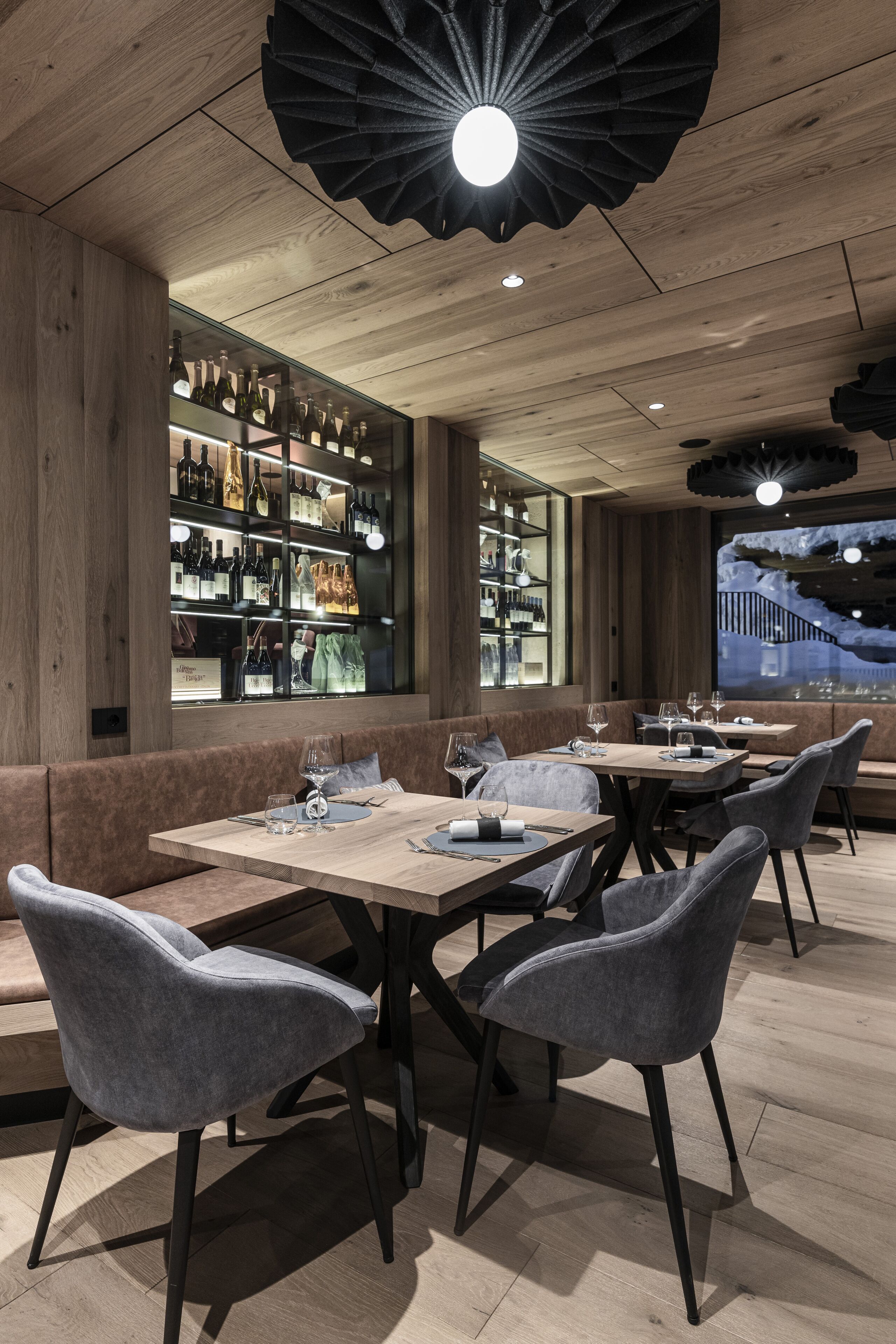 En restaurang med träpanel på väggarna, en bardisk med vinflaskor och olika typer av sittplatser.