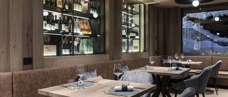 Een restaurantinterieur met houten paneelwanden, een bar met wijnflessen en zithoekjes.