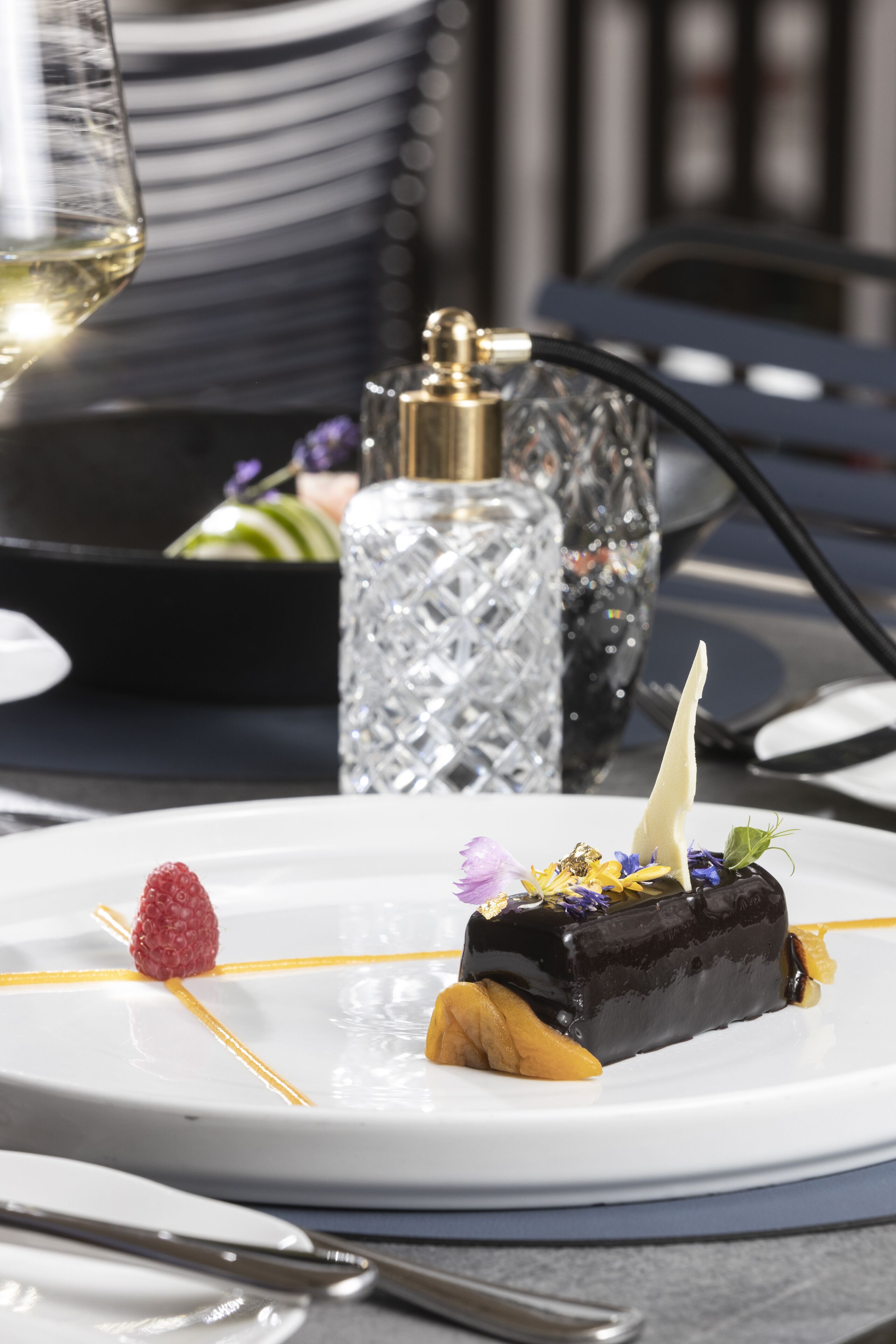 Un piattino con mousse al cioccolato, lampone e decorazioni su un piatto bianco.