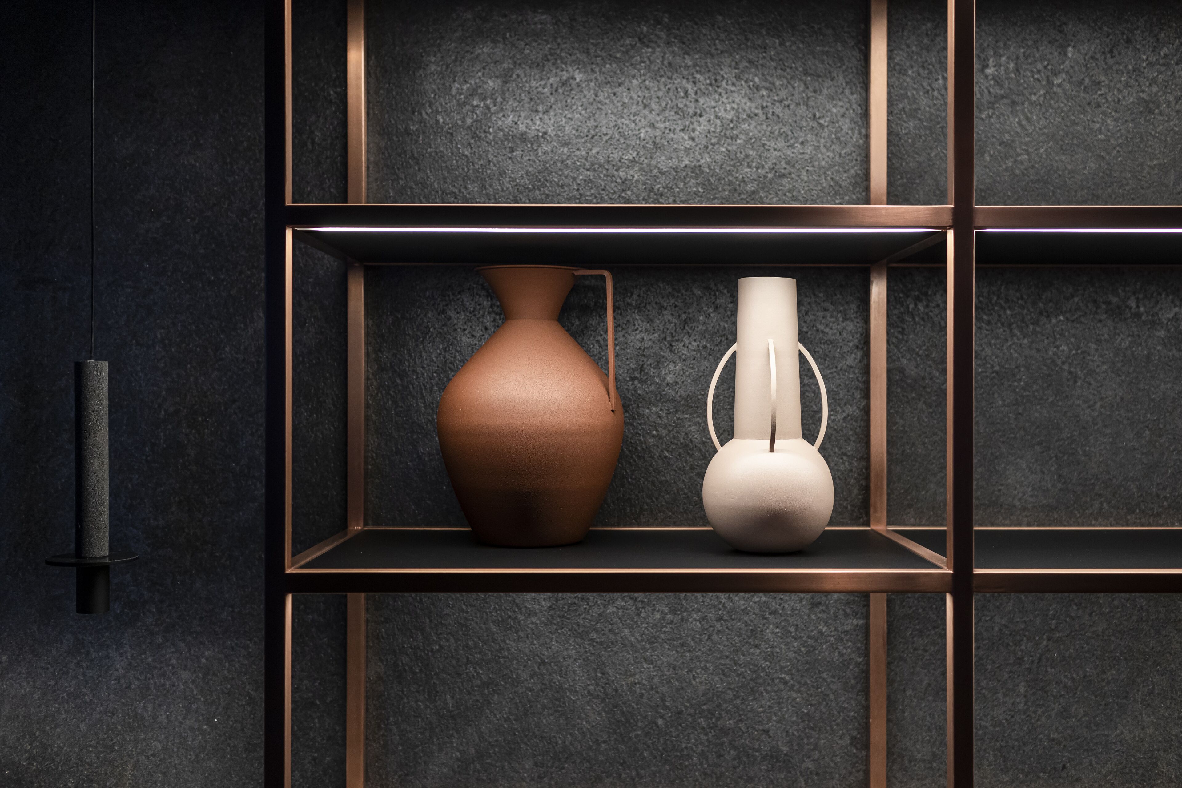A dark wall with a shelf containing two vases.