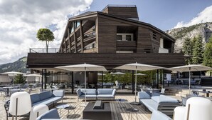 Un espacio exterior moderno con sillones de descanso y sombrillas, una terraza de madera y un edificio con balcones.