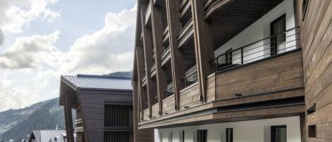A modern building with a wooden deck, outdoor seating, and a view of the mountains.
