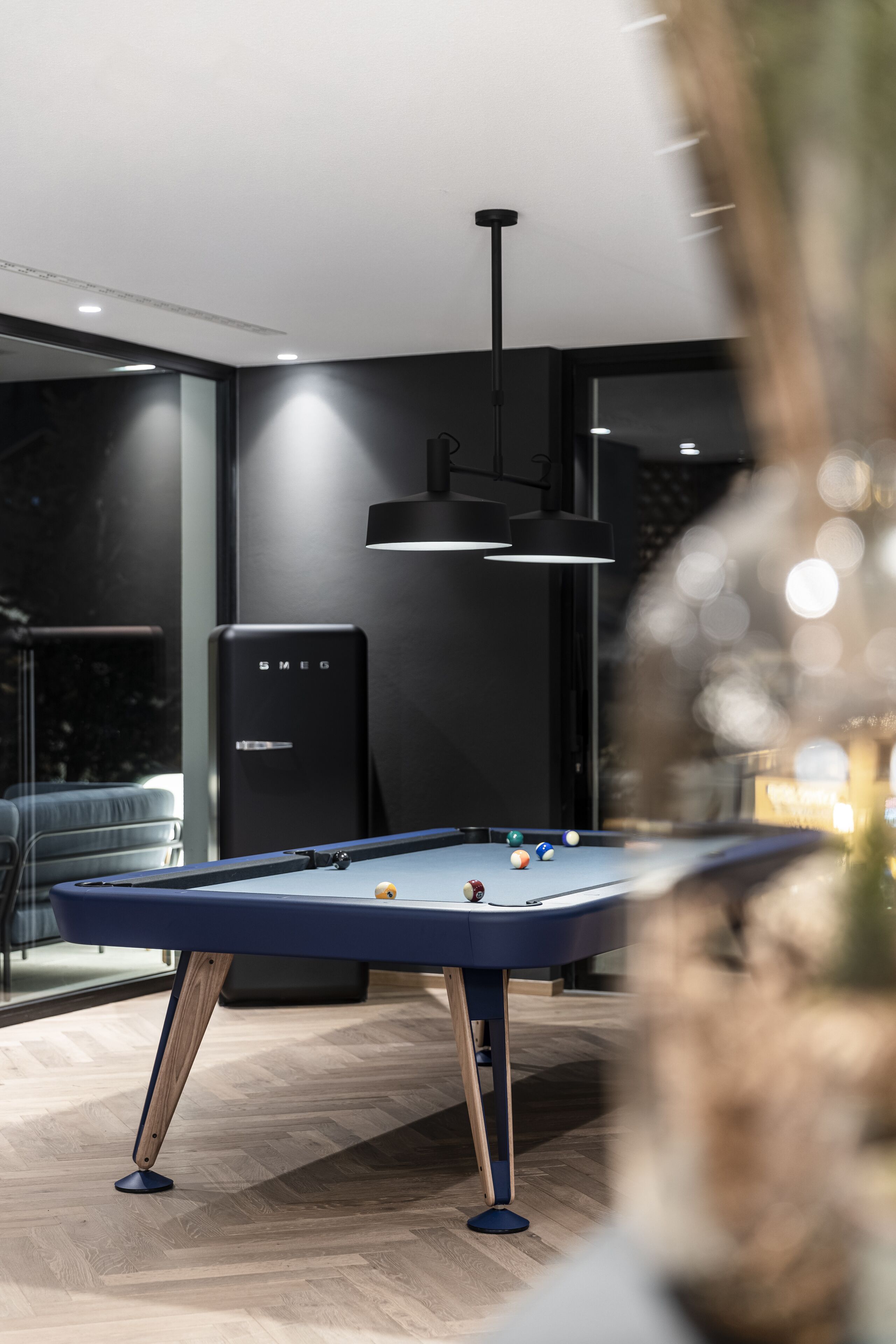 A pool table in a modern room with a large window, a black speaker, and a hanging light fixture.