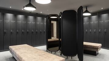 Un vestiaire moderne doté de plusieurs casiers, d’un banc et d’un miroir.