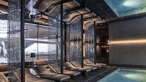 Una piscina interior con paredes de vidrio, sillas de descanso y un diseño de techo moderno.