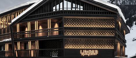 Un hôtel doté d’une enseigne bien visible indiquant « LINDER Cycling Hotel » et présentant une architecture moderne avec de grandes fenêtres et des poutres en bois.