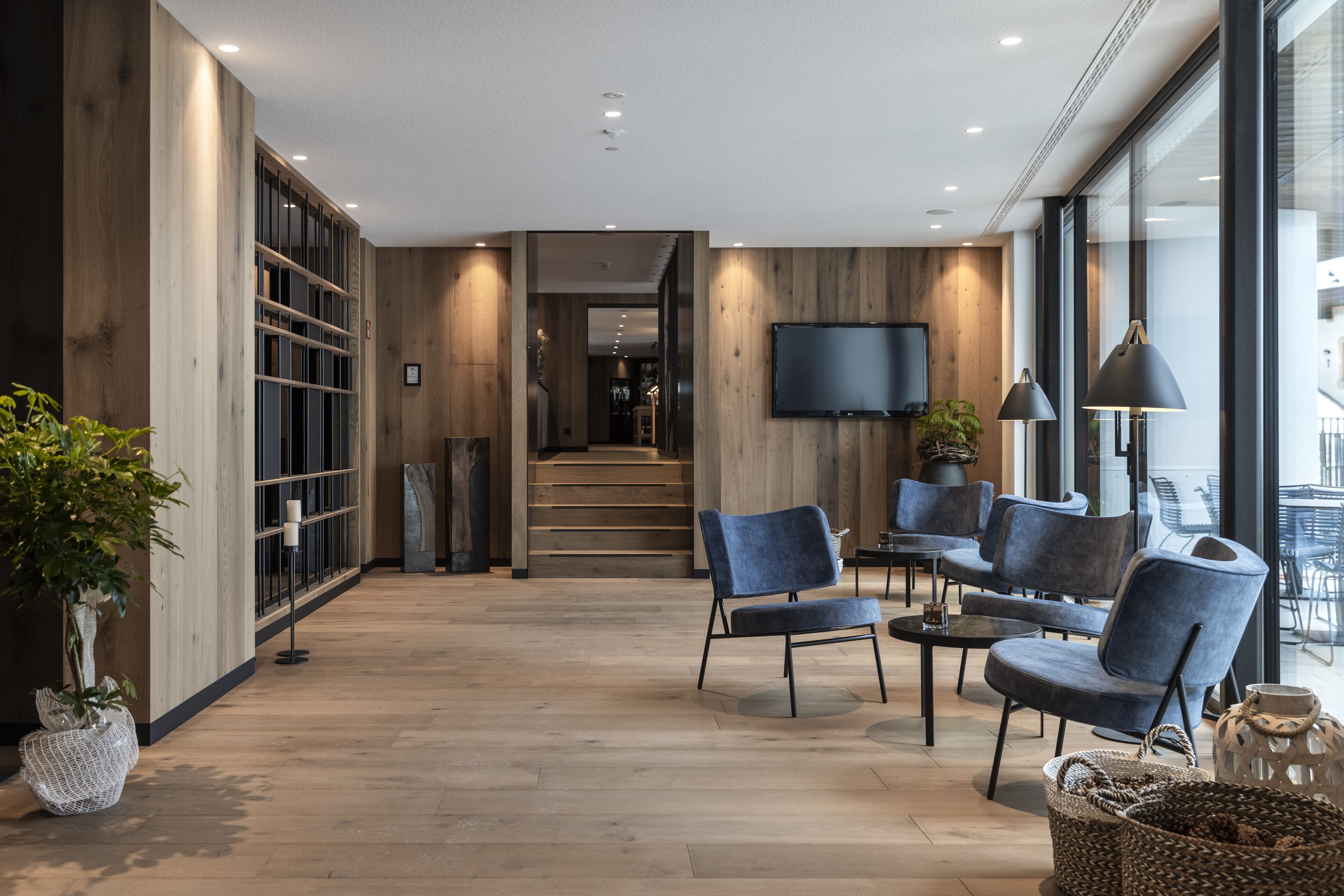 A modern interior with wooden flooring, a TV mounted on the wall, and a seating area with blue chairs and a coffee table.