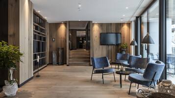 A modern interior with wooden flooring, a TV mounted on the wall, and a seating area with blue chairs and a coffee table.
