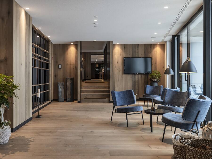A modern interior with wooden flooring, a TV mounted on the wall, and a seating area with blue chairs and a coffee table.