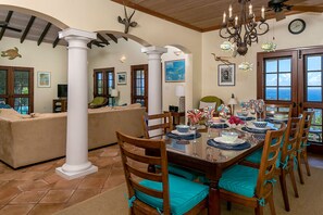 A dining area with a wooden table set for six, surrounded by chairs with teal cushions.