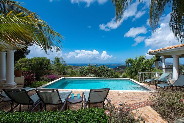 A rectangular swimming pool with a view of the ocean and hills in the background.