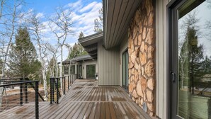 A modern house with a wooden deck, stone exterior, and large sliding glass doors. - RMR: Hal`e Teton Home in Teton Village (Teton Village)
