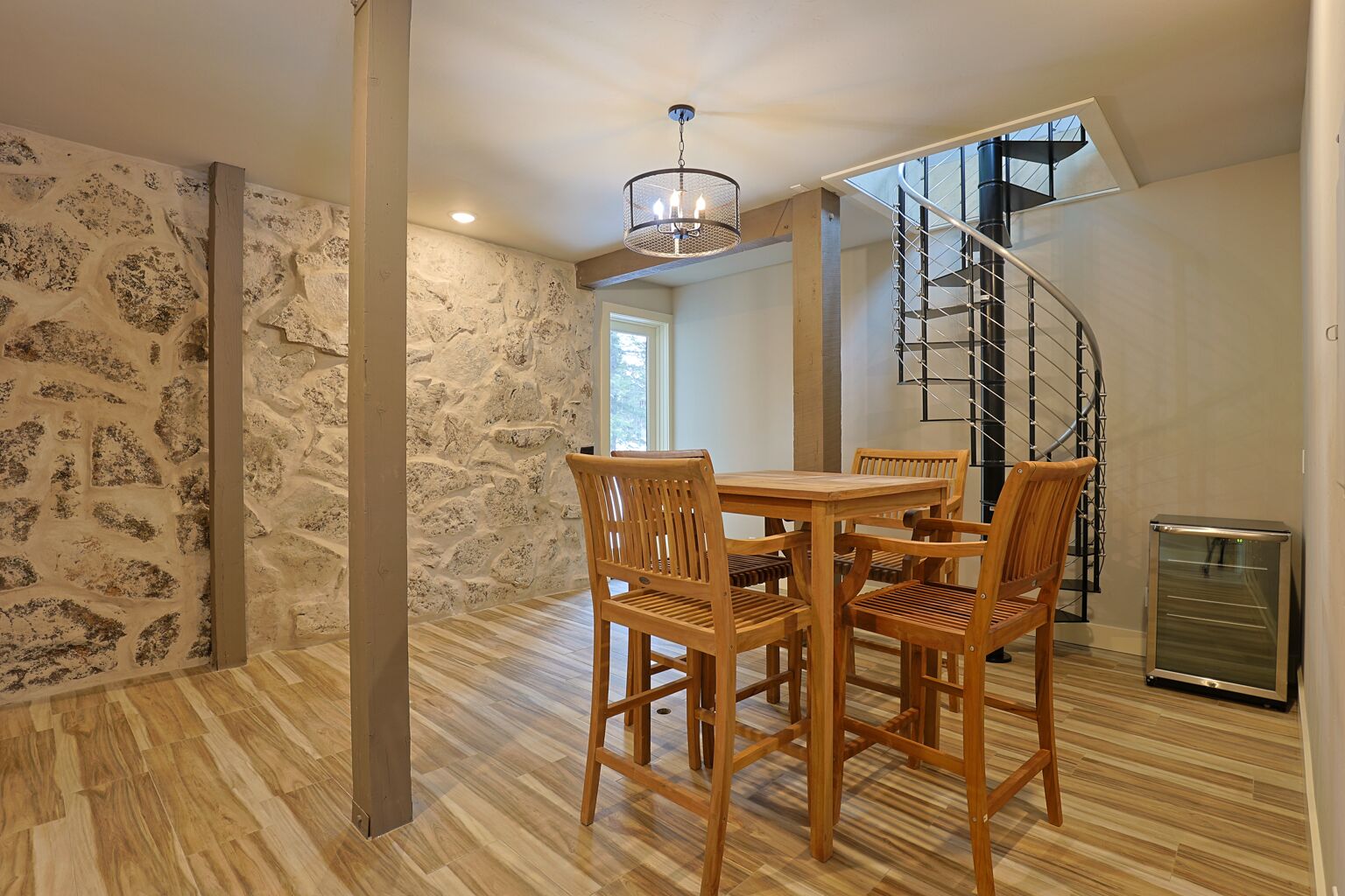 A dining area with a wooden table and chairs, a chandelier, a stone wall, and a spiral staircase.