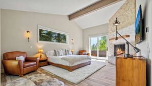 A spacious bedroom with a large bed, a leather armchair, a fireplace, and a TV mounted on the wall. - RMR: Hal`e Teton Home in Teton Village (Teton Village)