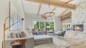 A spacious living room with a fireplace, large windows, and a high ceiling with exposed beams. - RMR: Hal`e Teton Home in Teton Village (Teton Village)