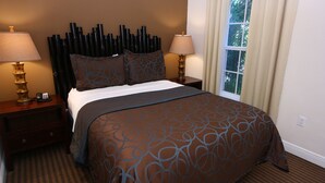 Une chambre d’hôtel avec un grand lit, deux tables de chevet avec des lampes, une fenêtre avec des rideaux et une couvre-lit à motifs.