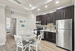 A modern kitchen with dark cabinets, stainless steel appliances, and a dining area with white chairs and a round table.