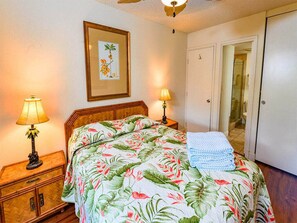 A bedroom with a bed, two bedside lamps, a framed picture on the wall, and a door leading to a bathroom. - Highly Upgraded West Maui Condo! WiFi, Modern Kitchen, Lanai–Kamaole Sands 9304 (KIHEI)