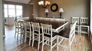 A dining area with a large wooden table surrounded by white chairs, a chandelier, and a wall clock. - FamilyMemoryMaker!,8 MASTERS,MovieRoom,OceanViews,Pool,HotTub,Grill,StarlinkWiFi (Corolla)
