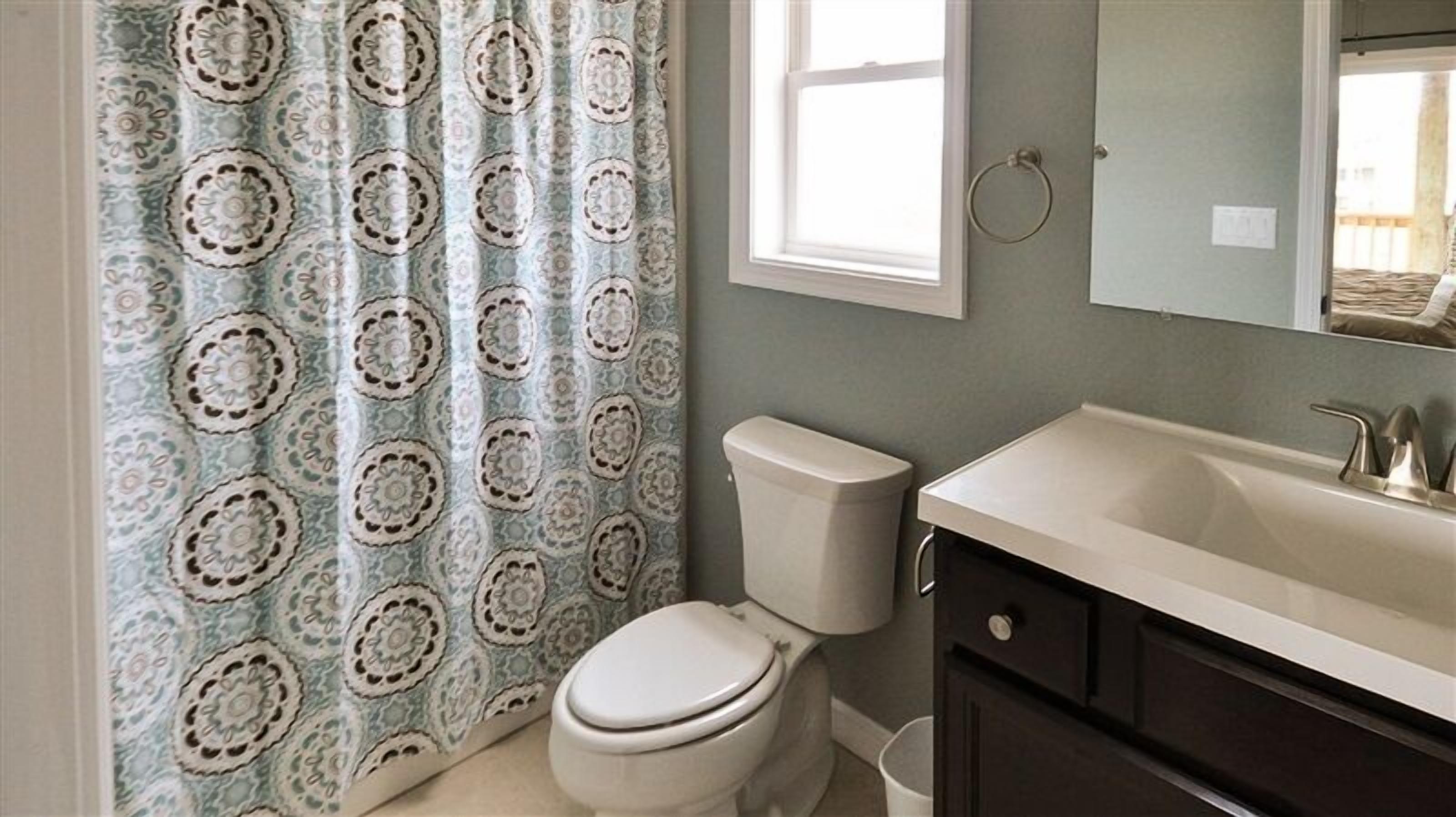 Ein Badezimmer mit gemustertem Duschvorhang, Toilette, Waschbecken mit Spiegel und Handtuchhalter.