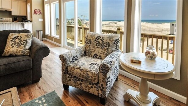 A living room with a sofa, armchair, and round table with a decorative item. Large windows offer a view of the beach. - FamilyMemoryMaker!,8 MASTERS,MovieRoom,OceanViews,Pool,HotTub,Grill,StarlinkWiFi (Corolla)