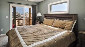 A bedroom with a large bed, a nightstand with a lamp, a window, and a view of buildings outside. - FamilyMemoryMaker!,8 MASTERS,MovieRoom,OceanViews,Pool,HotTub,Grill,StarlinkWiFi (Corolla)
