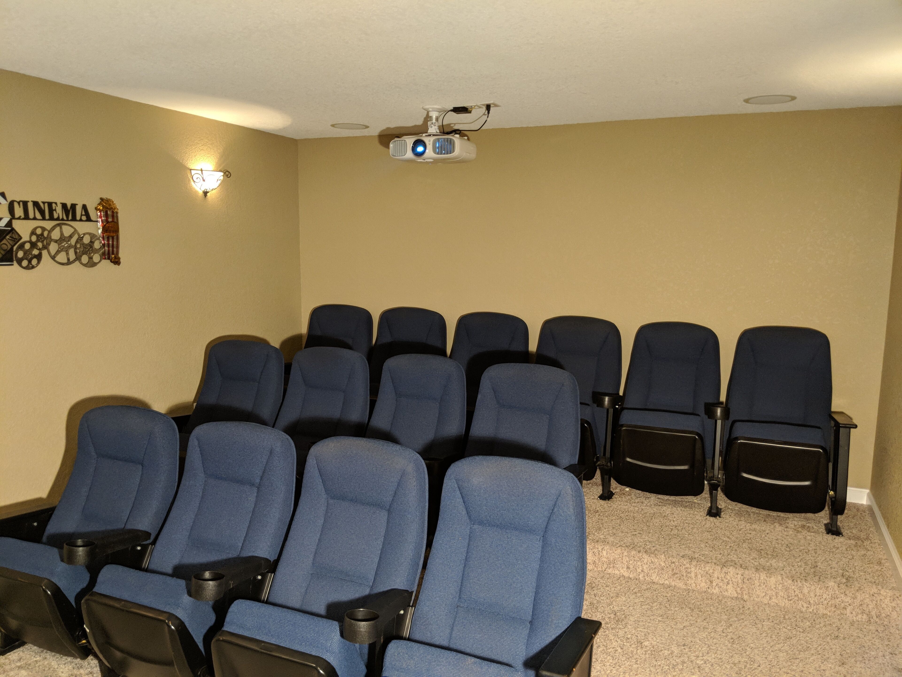 Une salle de cinéma maison équipée d’un projecteur, de haut-parleurs fixés au mur et d’un panneau indiquant « CINÉMA ».