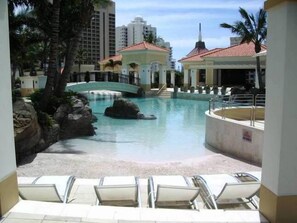 A pool area with lounge chairs, a bridge, and a building with a red roof. - Luxury Resort Chevron Renaissance in the heart of Surfers Paradise (Surfers Paradise)