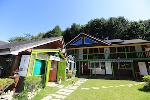A building with a green and brown facade, a visible entrance, and a stone pathway leading to the entrance.