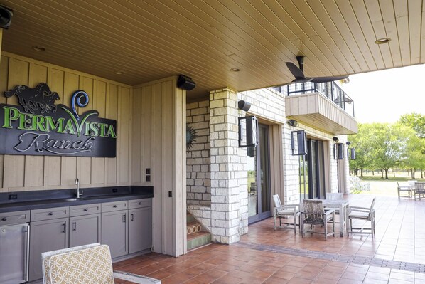 A covered outdoor patio area with a stone wall, a sign reading "PermaVista Ranch," and a dining table with chairs.