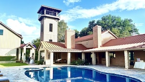 A pool area with stone tiles, a brick building with a tower, and a covered patio. - PermaVista Ranch & Resort- Experience A Luxury Texas Ranch (Brenham)