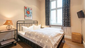 A bedroom with a bed, a nightstand, a lamp, a wall-mounted TV, a window with curtains, and a poster on the wall.