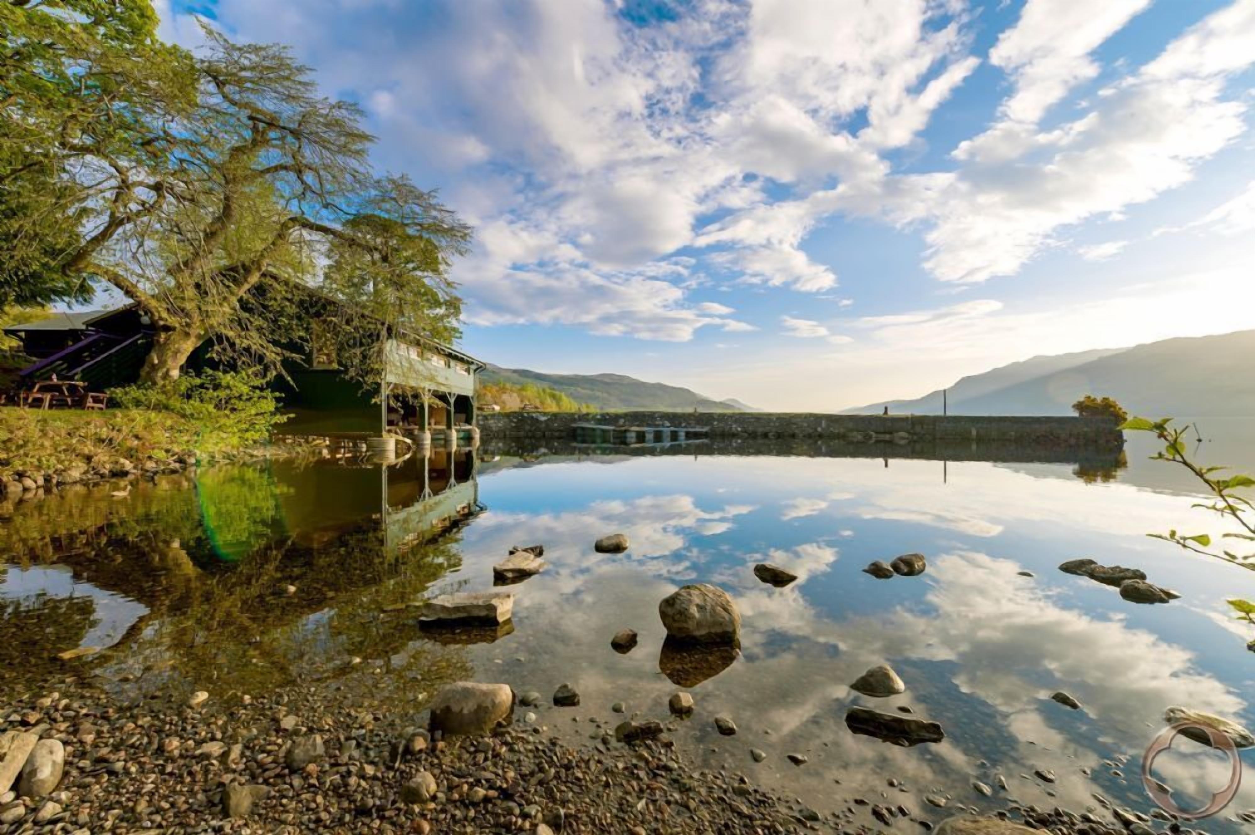Um lago calmo com um píer de madeira que se estende sobre a água, rodeado por rochas e árvores.