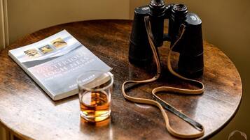 A book titled "The Guide to Mysterious Loch Ness" on a wooden table, accompanied by binoculars and a glass of amber liquid.