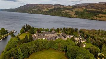 An aerial view of a historic castle with a large courtyard, surrounded by dense forest and a lake.