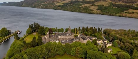 An aerial view of a historic castle with a large courtyard, surrounded by dense forest and a lake.