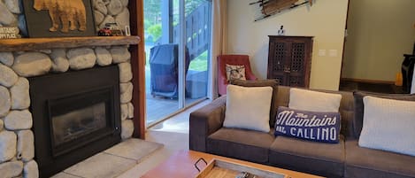 A living room with a stone fireplace, a sofa with decorative pillows, a wooden coffee table, and a stone wall.