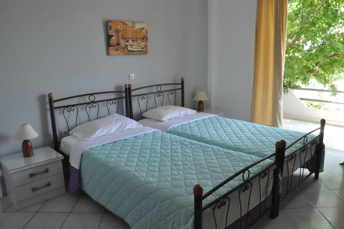 Una cama de matrimonio con colcha acolchada, dos mesitas de noche con lámparas, un cuadro en la pared y una ventana con vistas a zonas verdes.