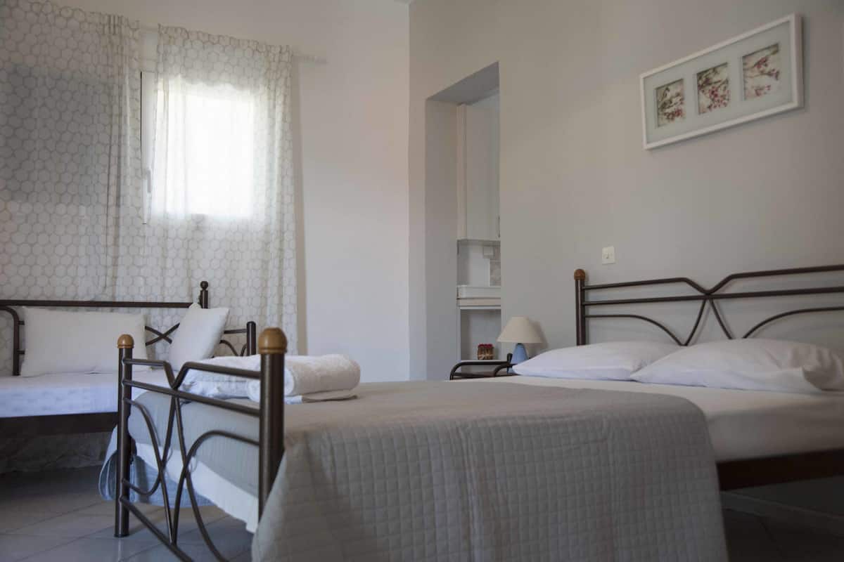 Habitación de hotel con dos camas, una ventana con cortina estampada, una mesita de noche con lámpara y un cuadro enmarcado en la pared.